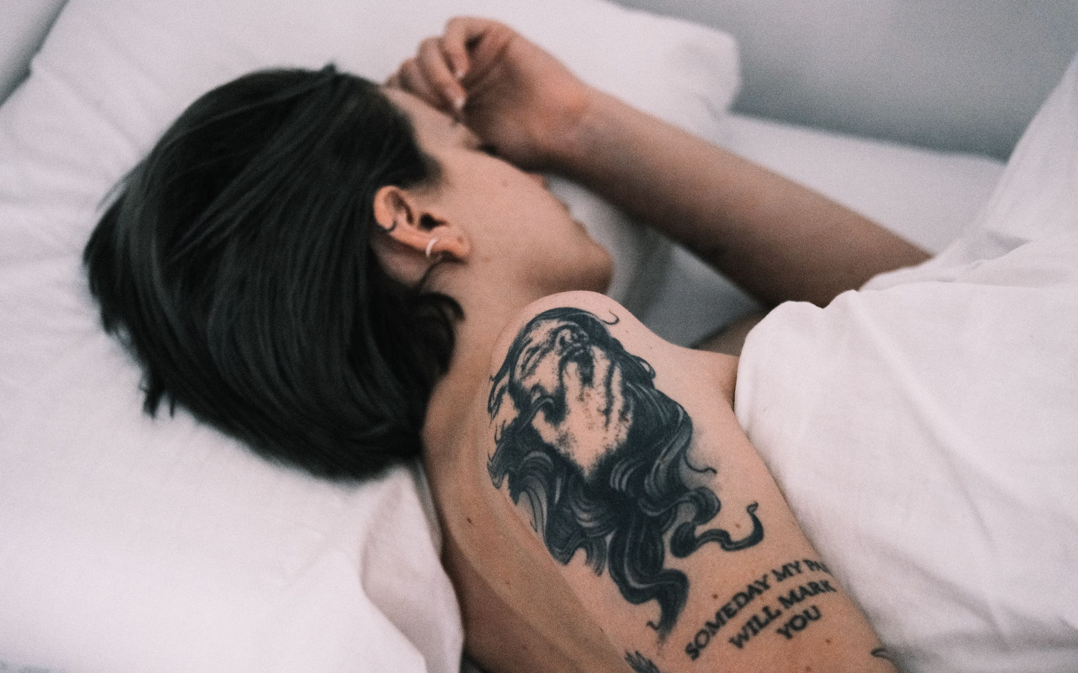 Bild av en person med tatueringar som sover naken i sängen